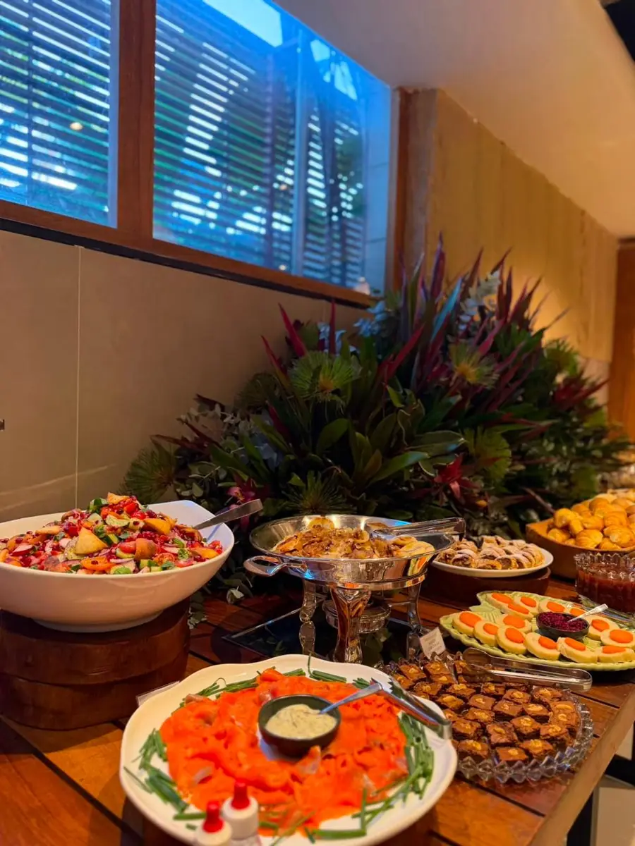 Buffet com salada, salmão defumado, canapés de legumes e doces, junto a um grande arranjo tropical