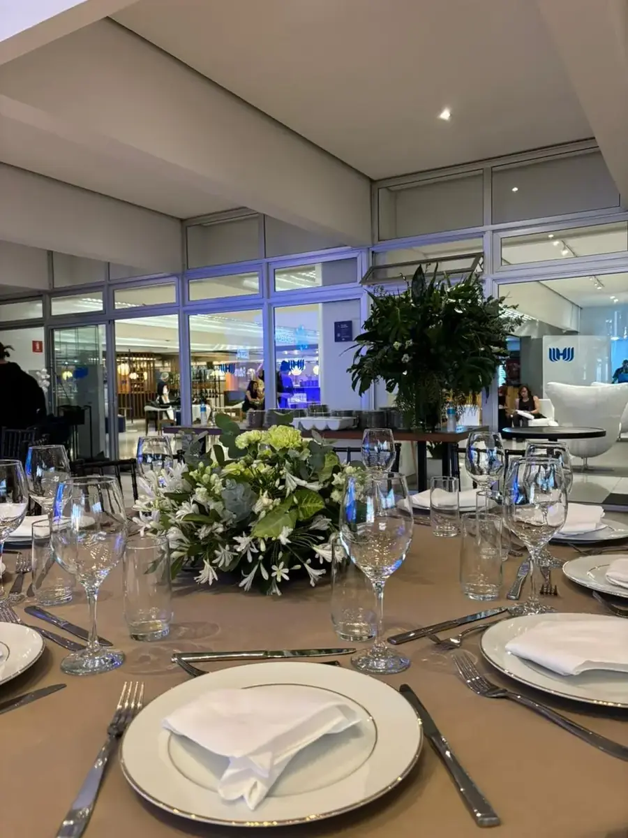 Mesa redonda posta com louça branca e arranjo verde, em evento diurno