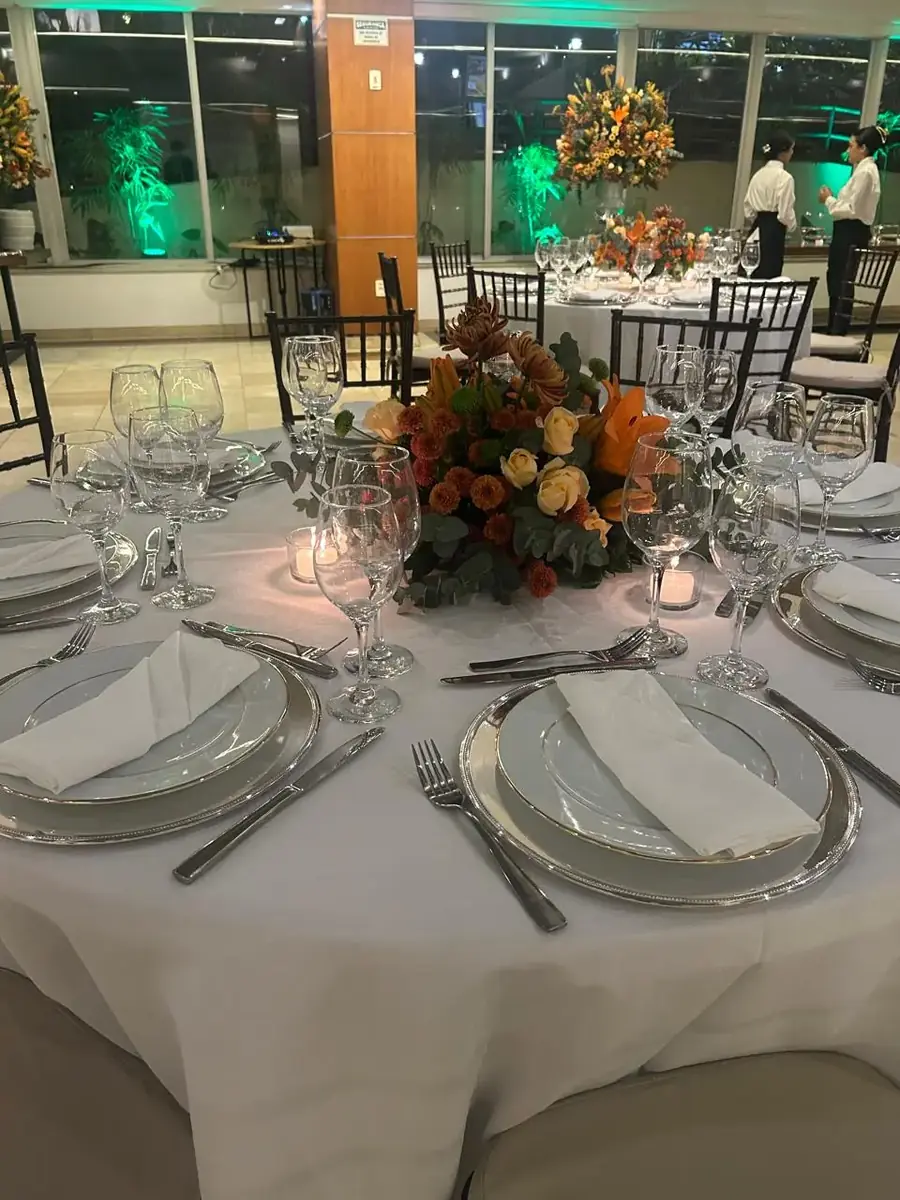 Mesa redonda posta para jantar de festa, com arranjo de flores laranja e velas